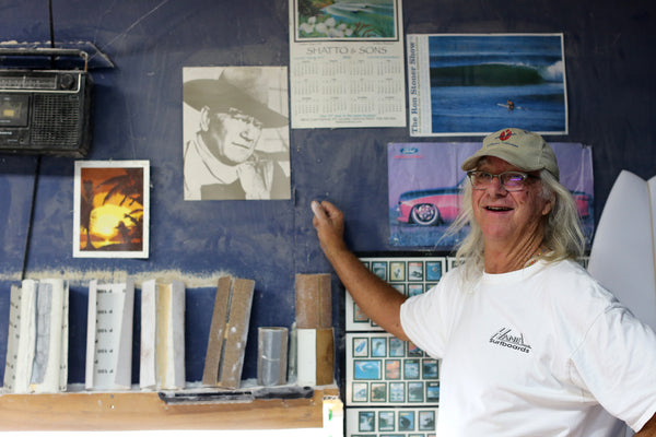 Gary Hanel in his surfboard shaping room looking at a picture of John Wayne